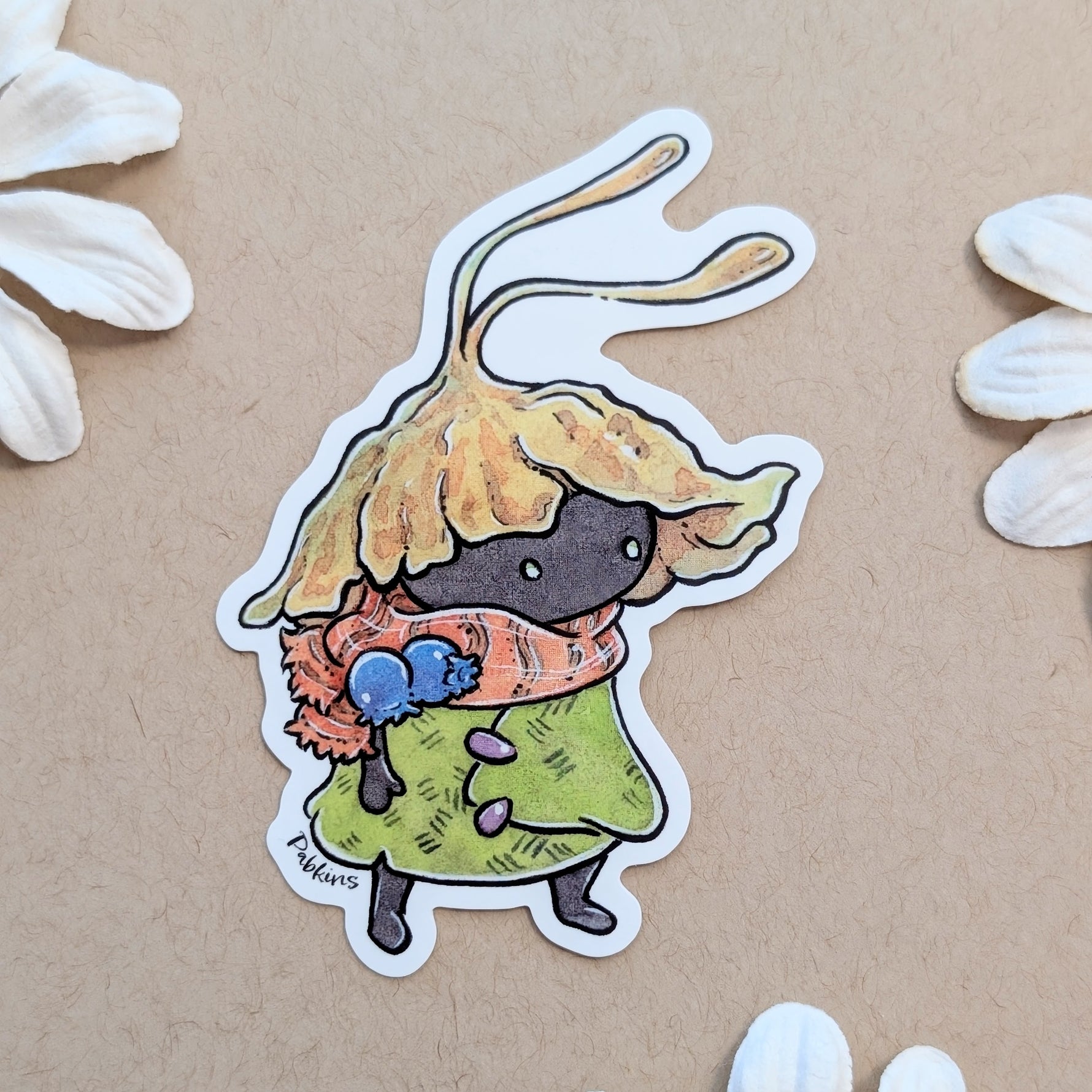 A die-cut sticker featuring a cute cartoon creature with a leafy yellow hat, green coat, and orange scarf