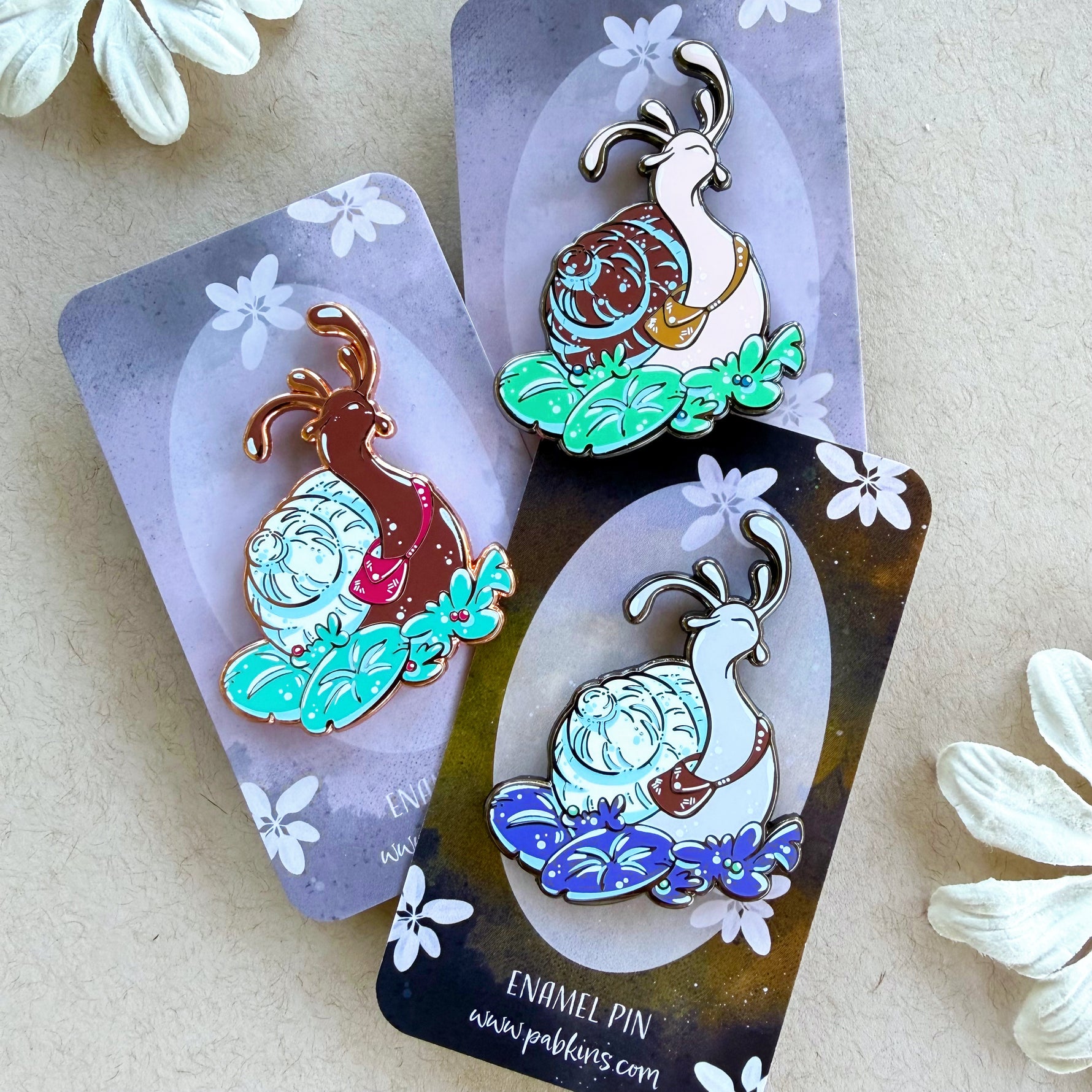 Photograph of 3 different colored snail enamel pins